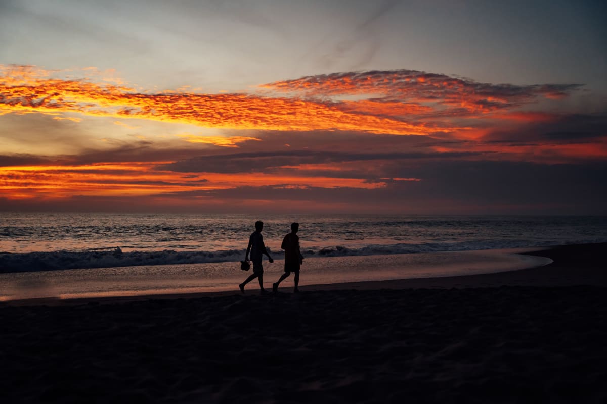Dos personas caminando por la playa de arena de Tulum México durante un vibrante atardecer
