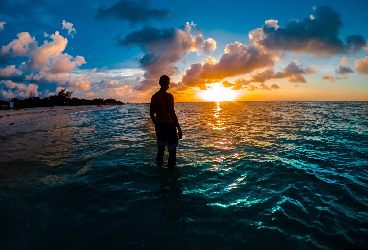 Person standing in the sea at sunset on Holbox beach with clouds lit orange over the water