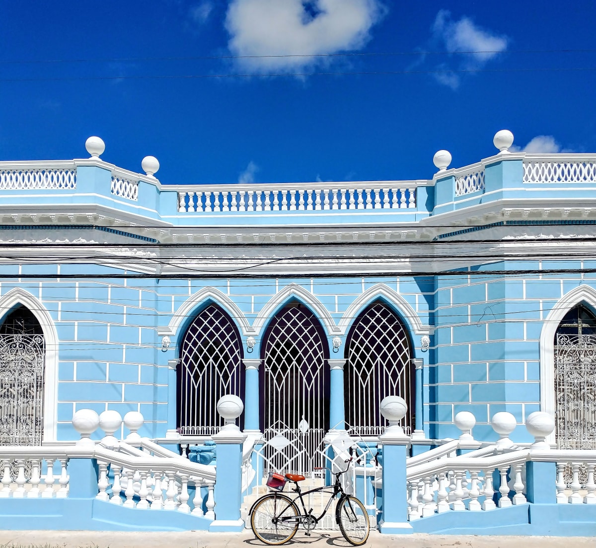 Pale blue mansion with pointed arched windows, white balustrades and a bicycle outside in Merida
