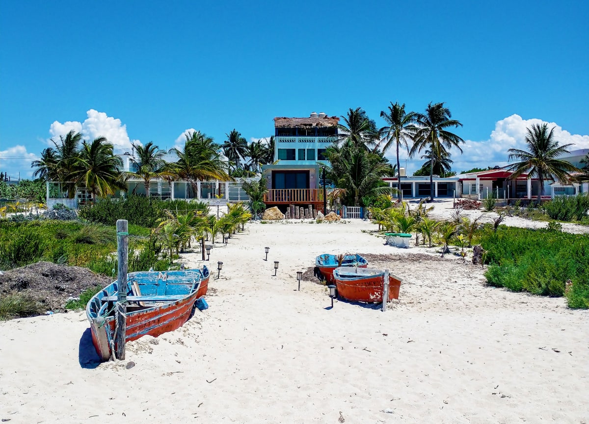 Lanchas de pesca de madera sobre la arena blanca frente a casas de playa y palmeras en la costa de Progreso, cerca de Mérida