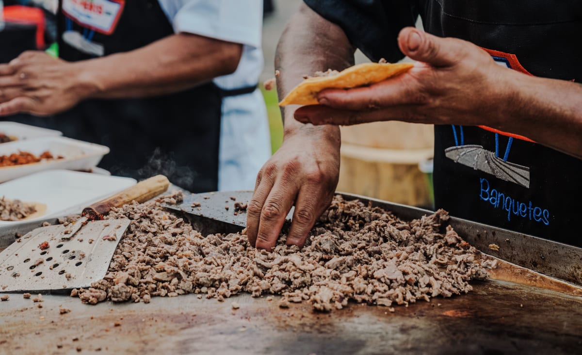 Vendeur garnissant une tortilla de viande grillée à un stand de tacos, la façon la moins chère de bien manger au Mexique