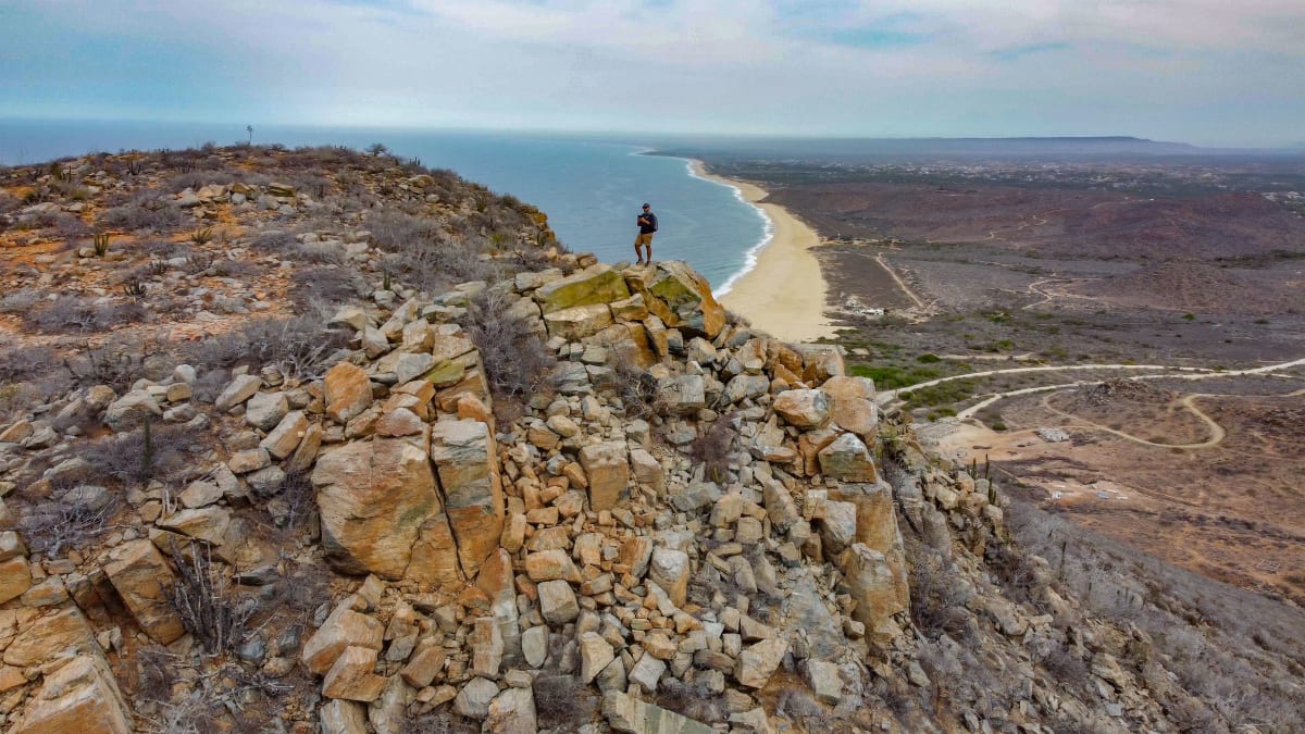 Hiker on a rocky hilltop above a long Pacific beach near Todos Santos