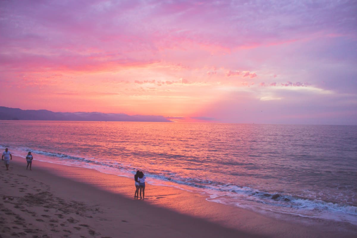 Coucher de soleil rose sur la baie de Banderas avec des promeneurs sur la plage de Puerto Vallarta
