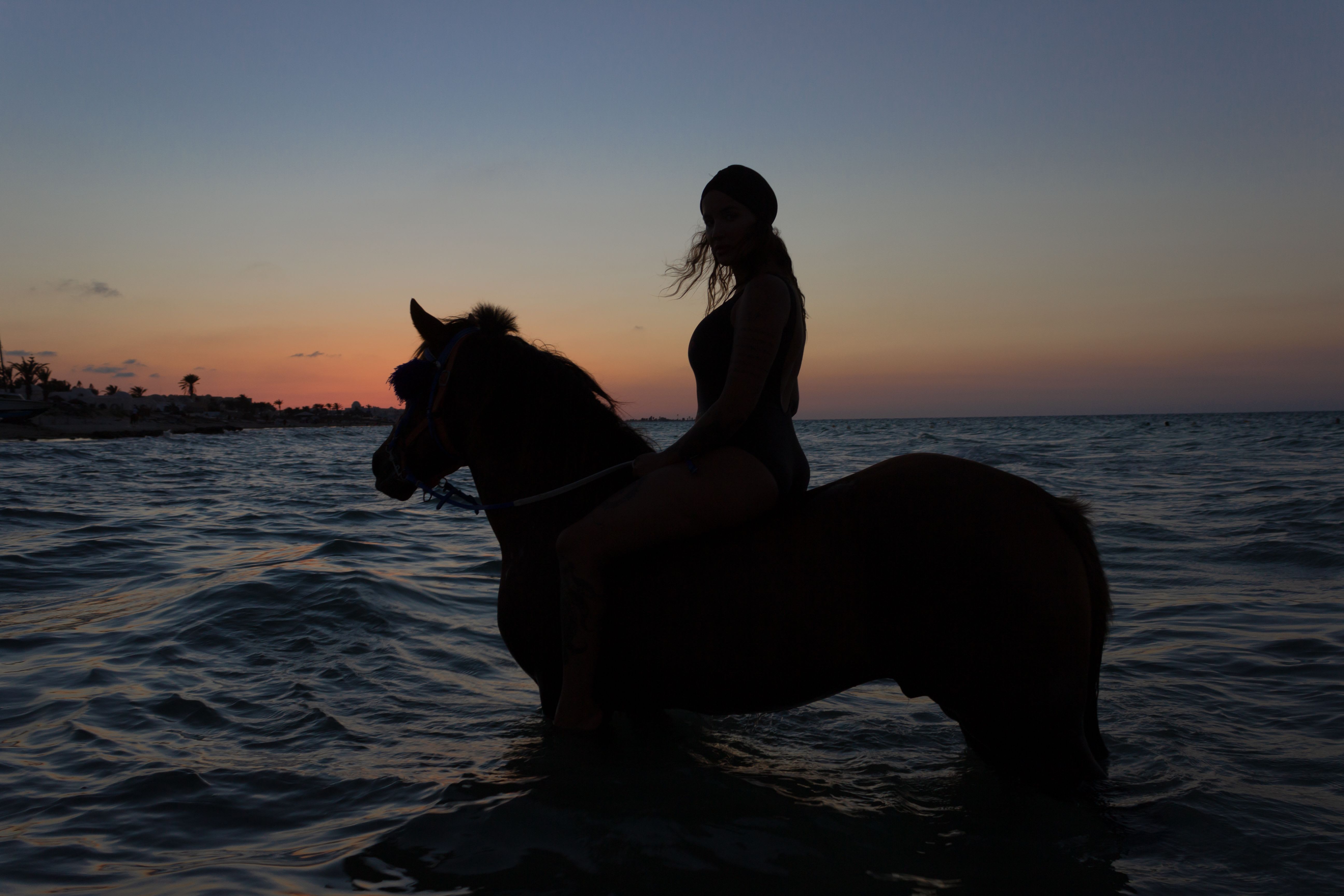 Horseback riders silhouetted against a vivid Caribbean sunset on the Tulum beach near the Zona Hotelera