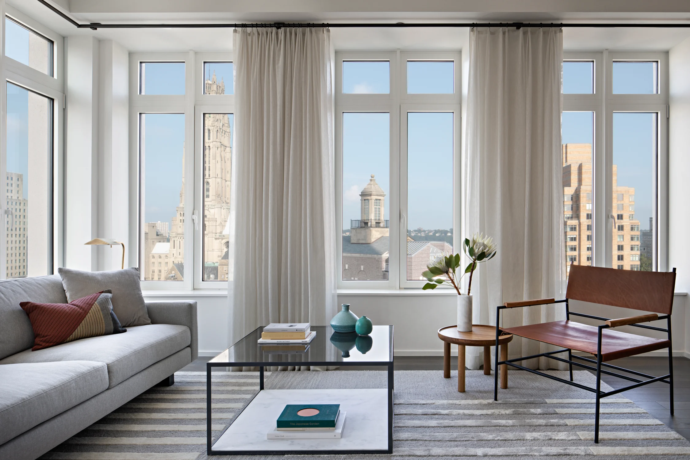living room, coffee table, windows, skyline view, chair, leather, vase, flowers, cushions, glass table top, side table, drapery