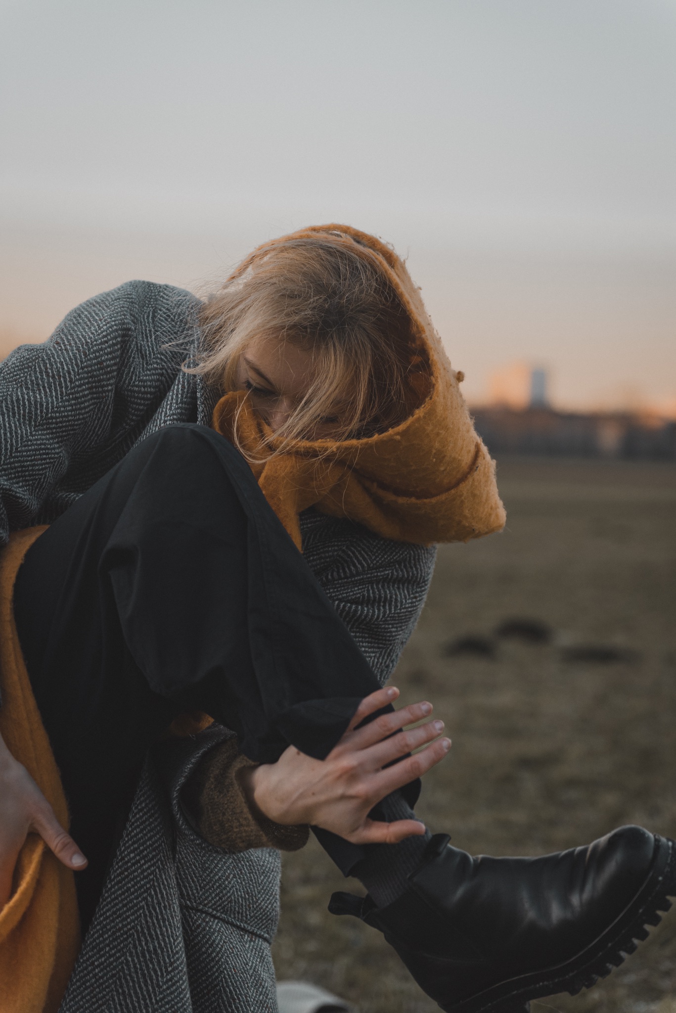 Katharina Ludwig in an orange scarf and grey coat, posed in a field at sunset