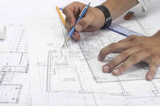 an engineer or architect's hands drawing and marking dimensions on detailed blueprints with a pen and ruler for engineering design