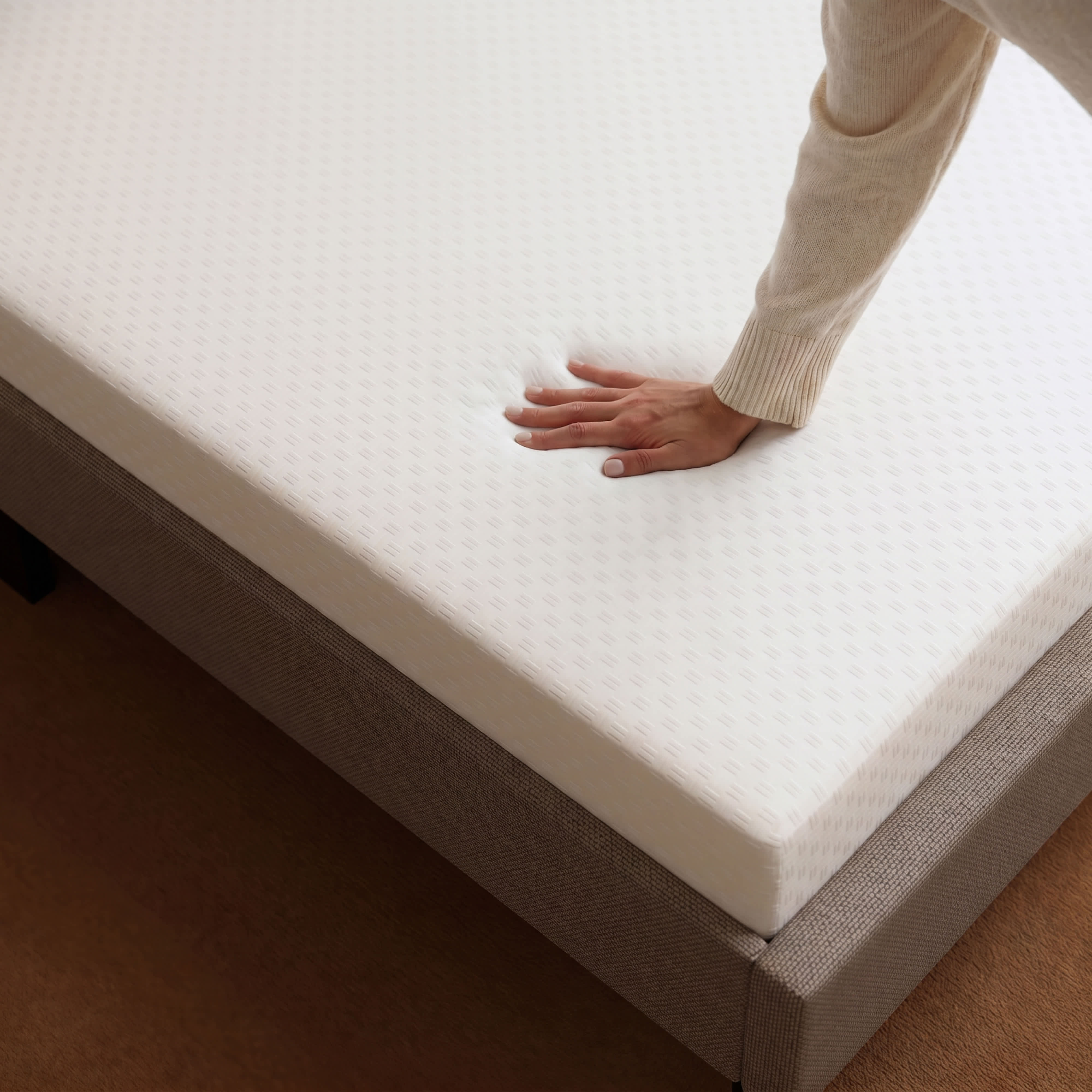 A hand presses into a white Memory Foam mattress, showing its soft, conforming texture