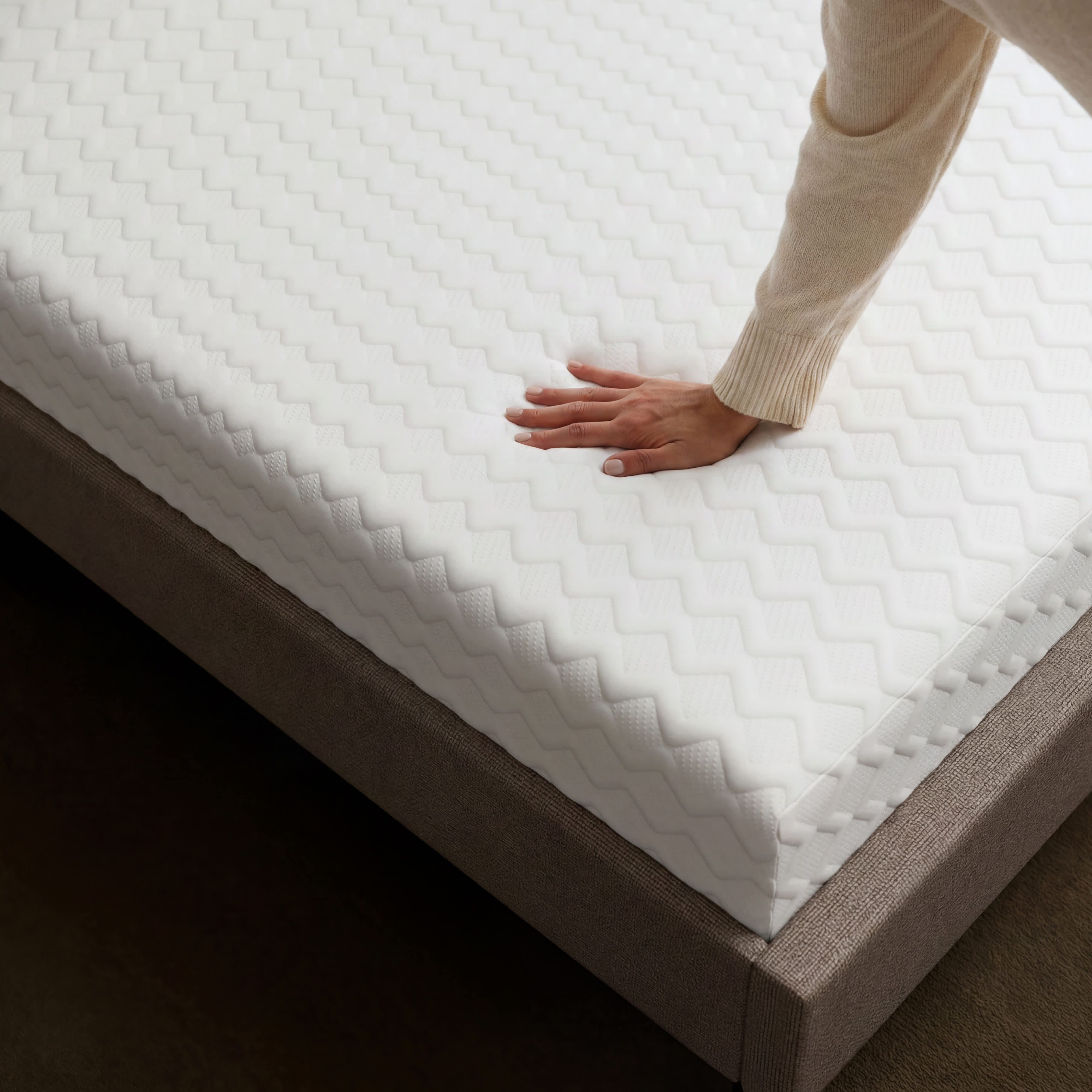 A hand presses into the textured white surface of a Memory Foam mattress on a bed frame