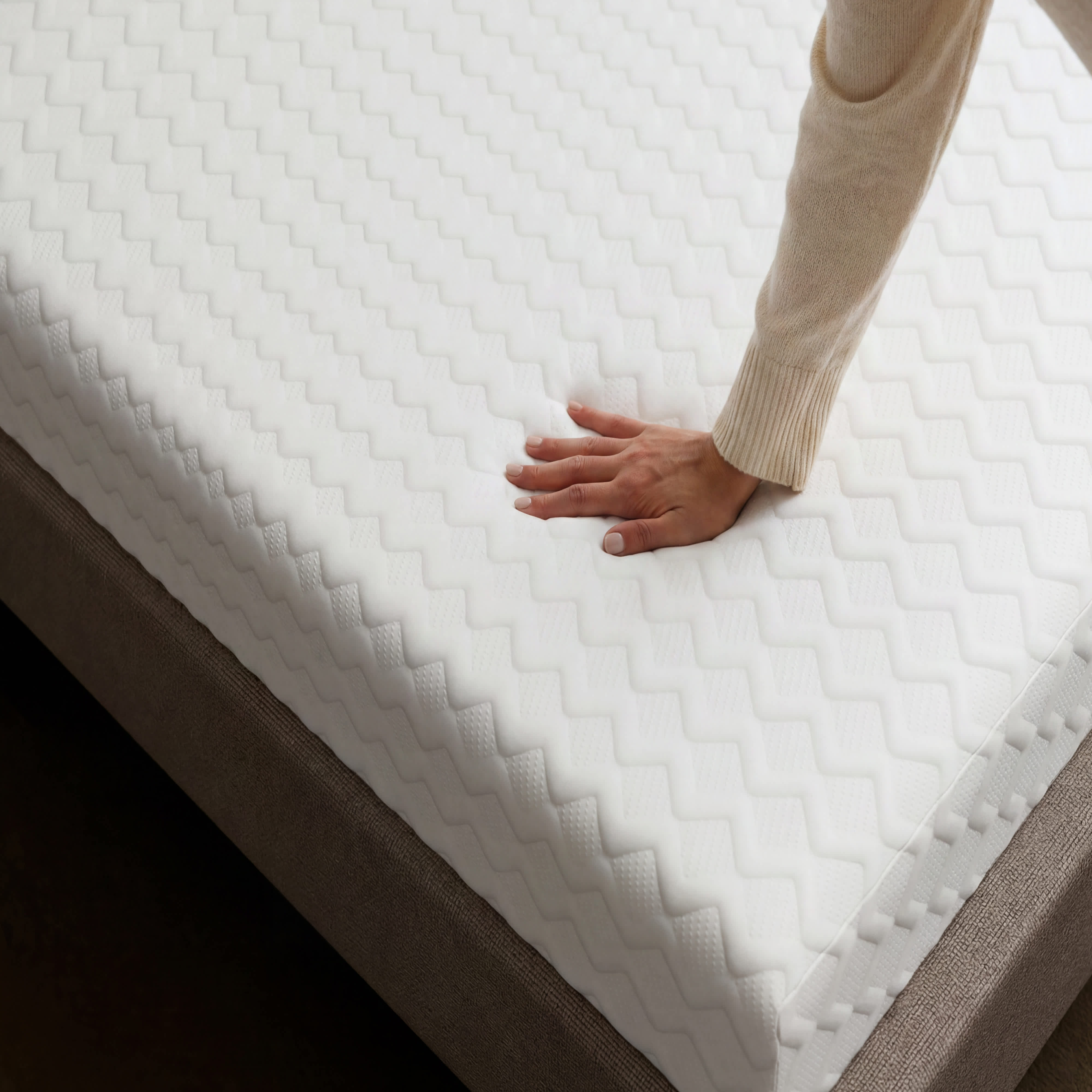 A hand presses into the white, textured surface of a Memory Foam mattress, showing its softness