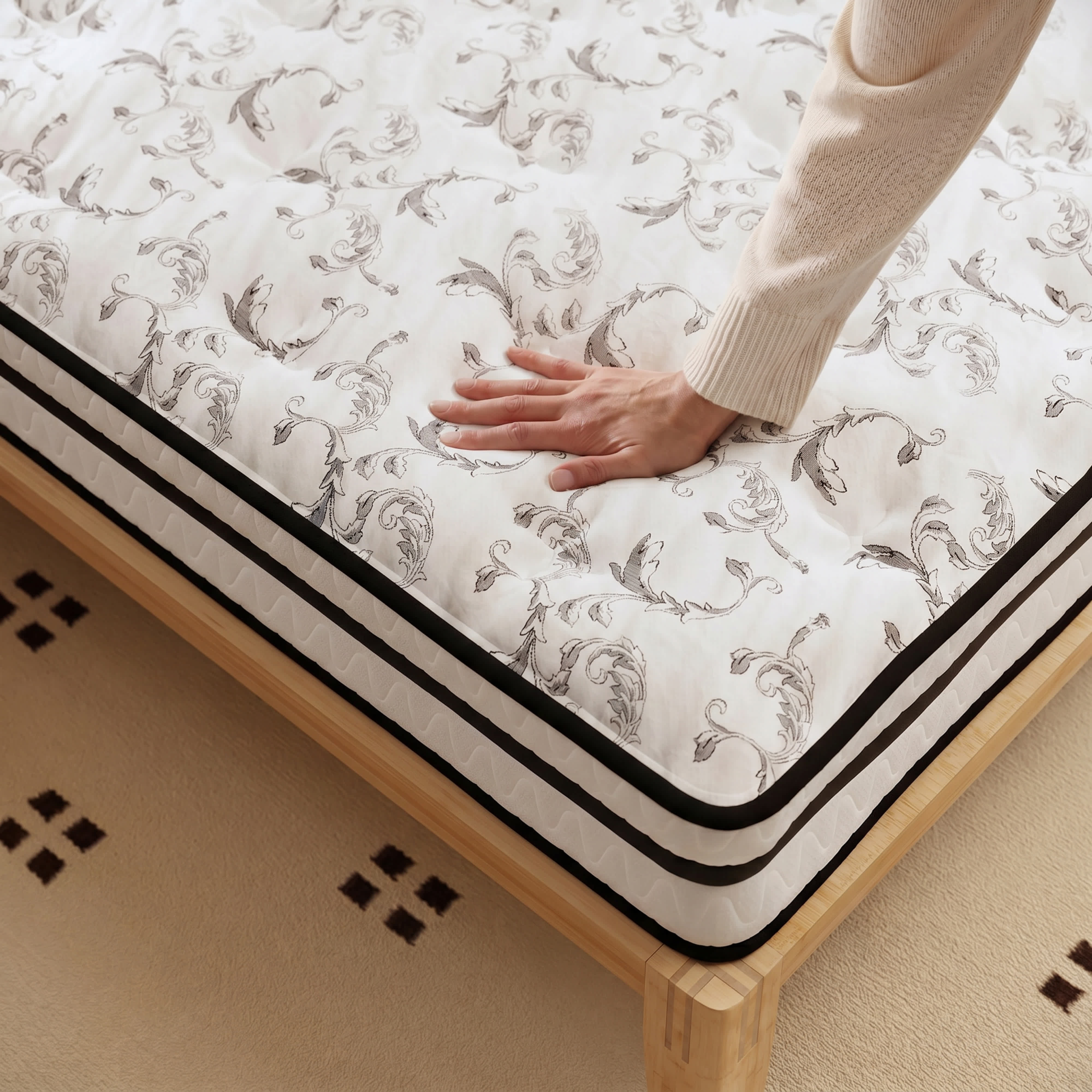 A hand presses on the patterned white surface of a hybrid mattress on a light wood bed frame