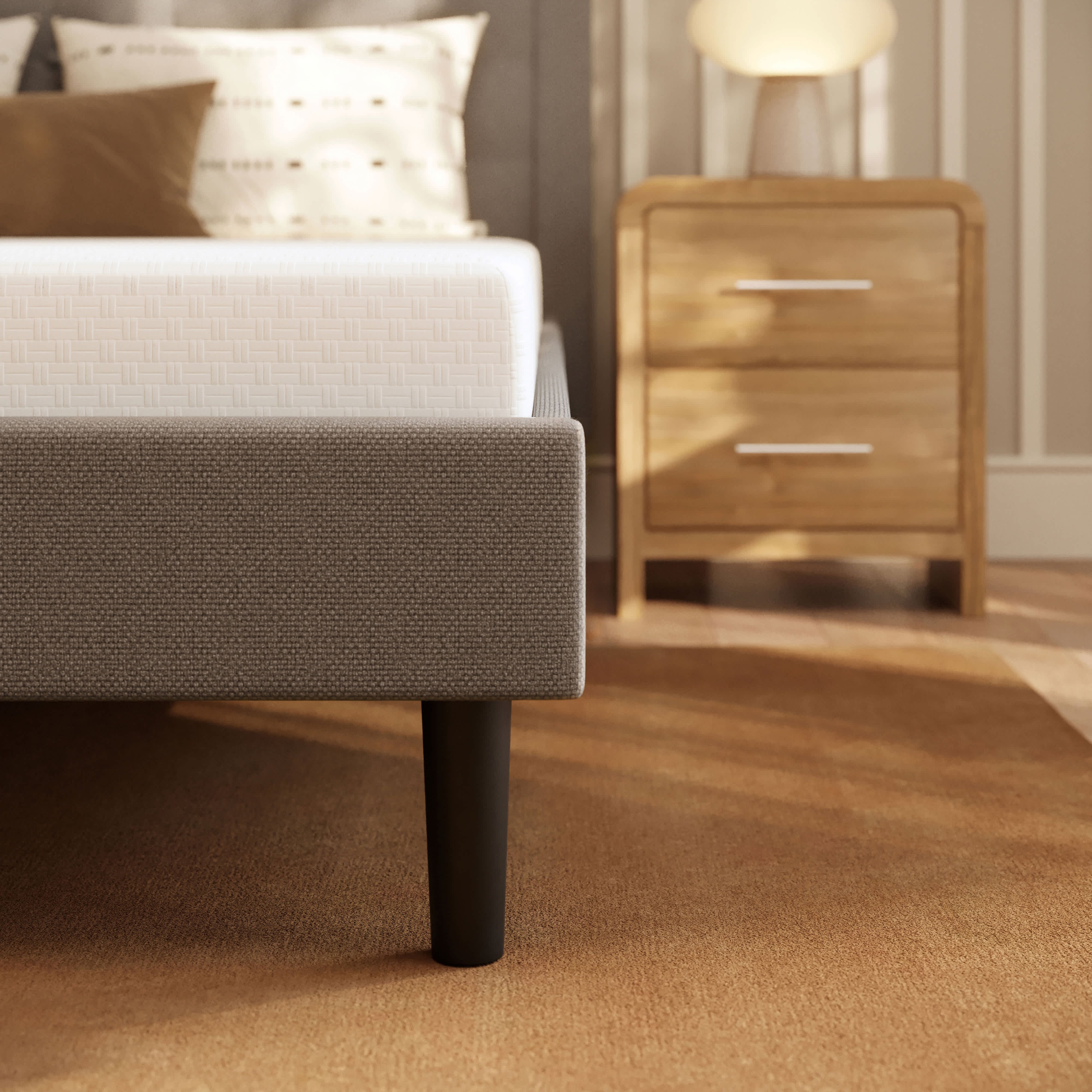 A close-up of a bed with a white Memory Foam mattress and a gray fabric frame, next to a wooden nightstand