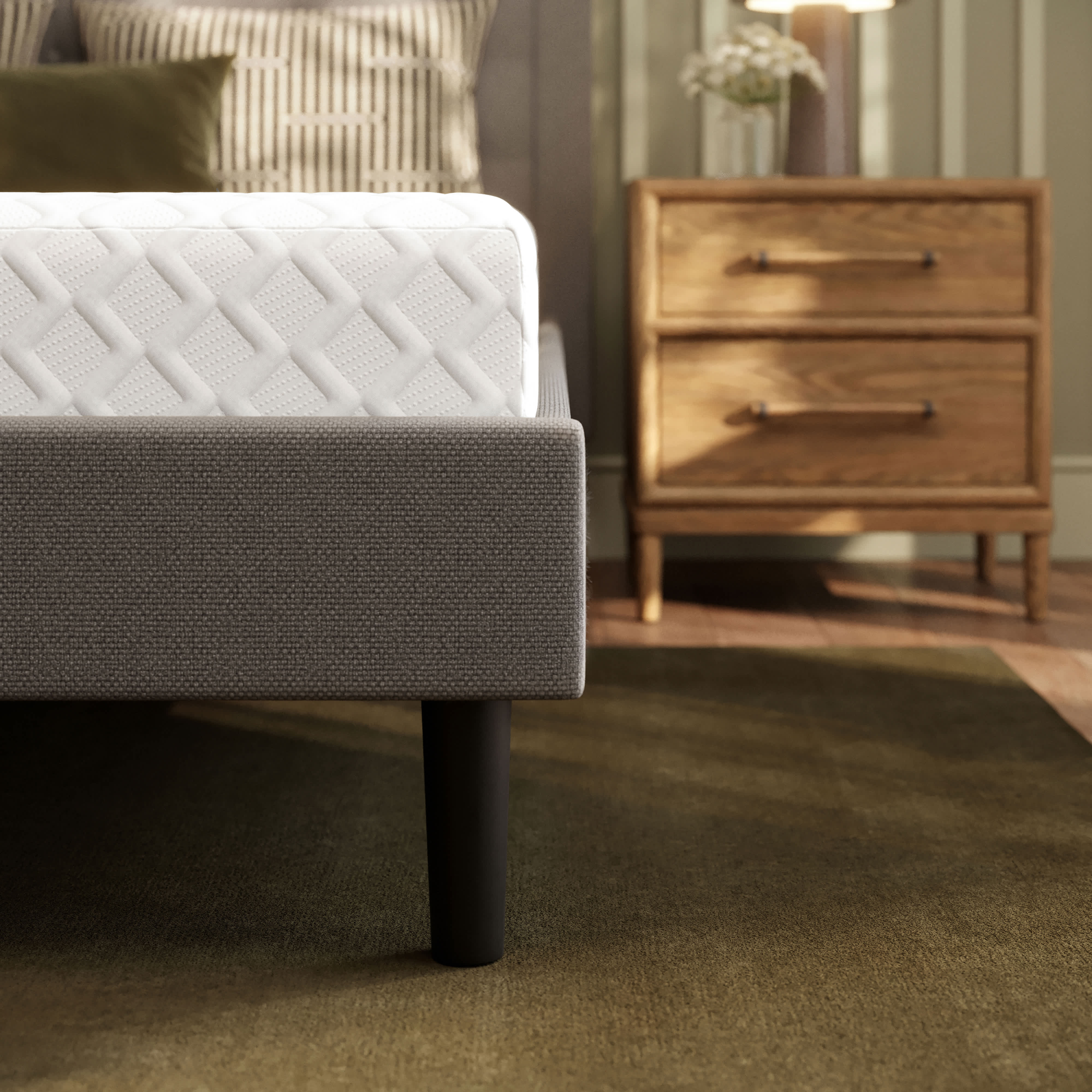 A Memory Foam mattress on a gray fabric bed frame with black legs, next to a wooden nightstand