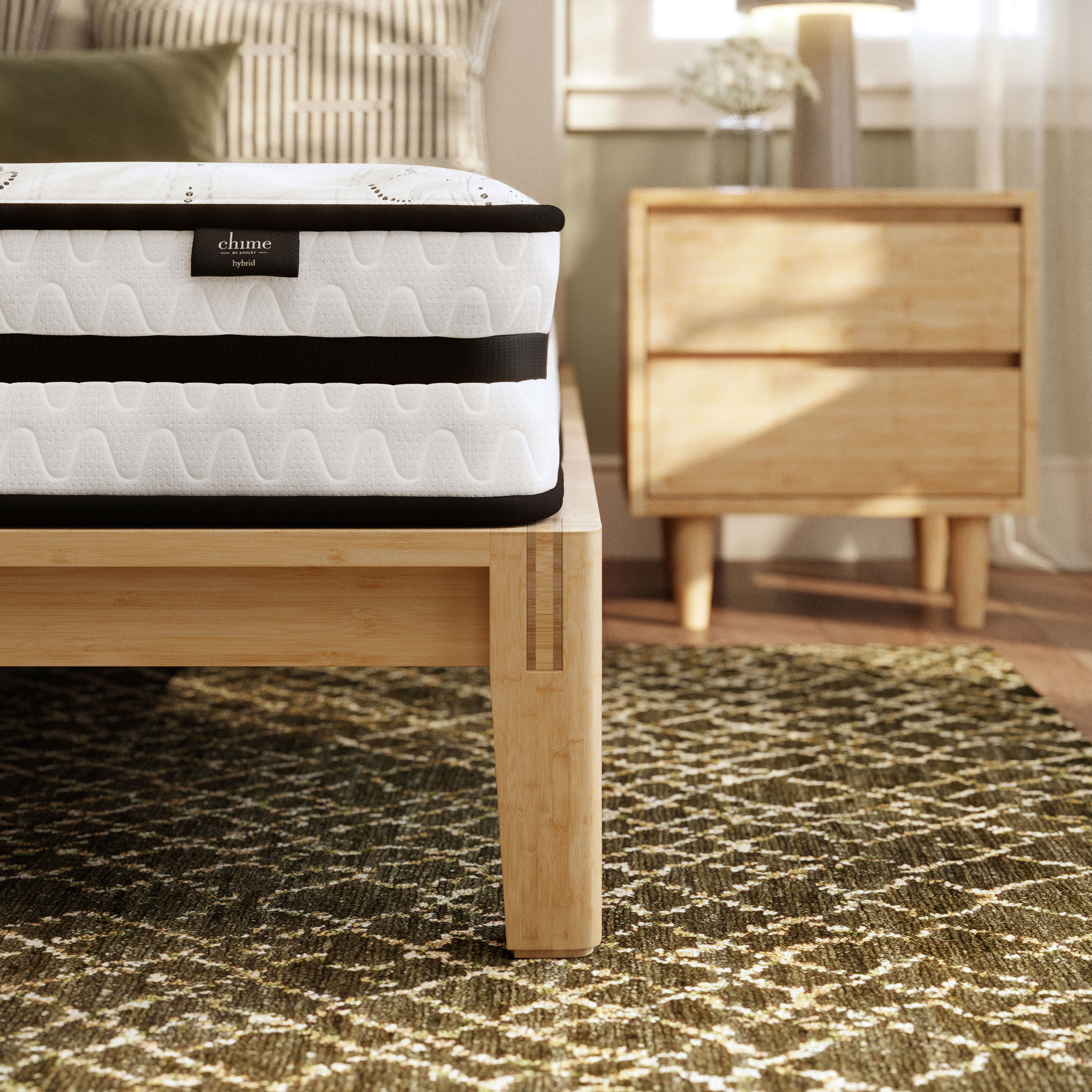 A Hybrid mattress on a light wood bed frame, with a patterned rug and nightstand in the background