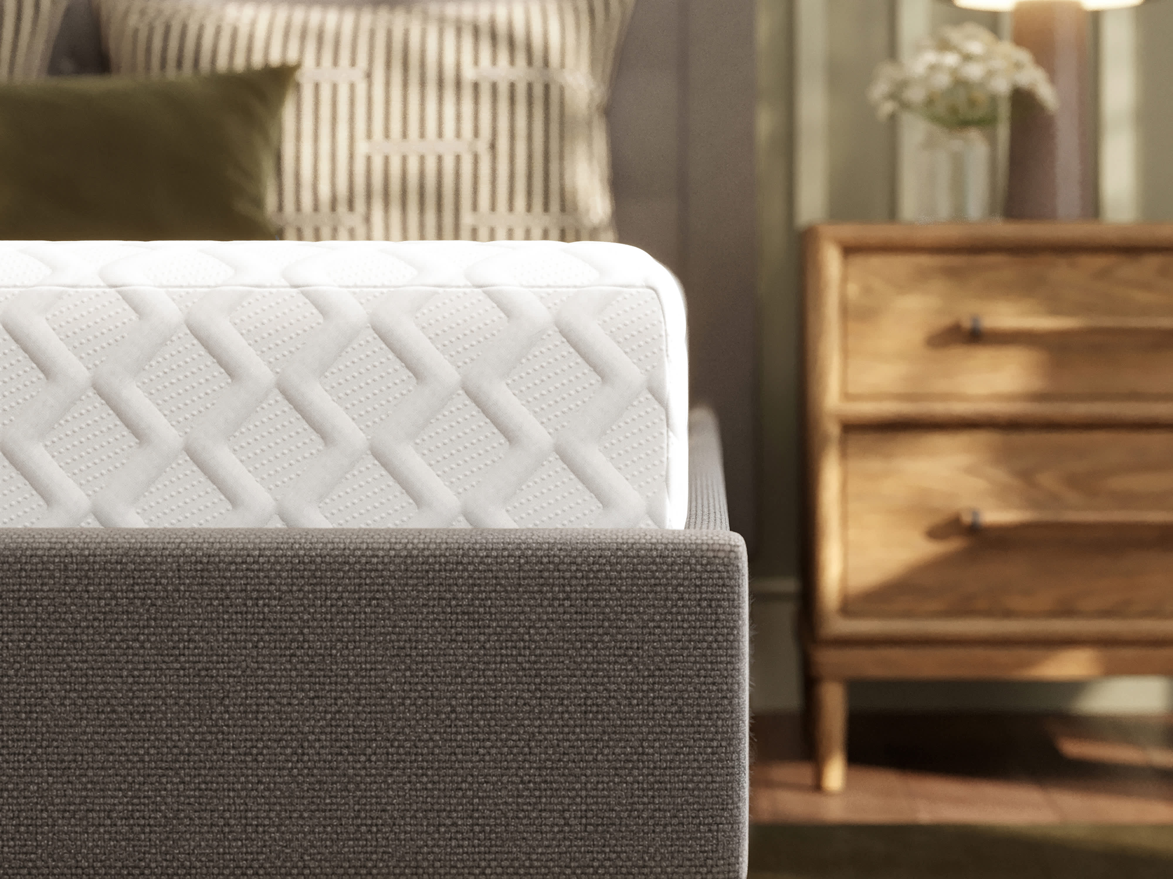 A memory foam mattress on a gray fabric bed frame with black legs, next to a wooden nightstand.