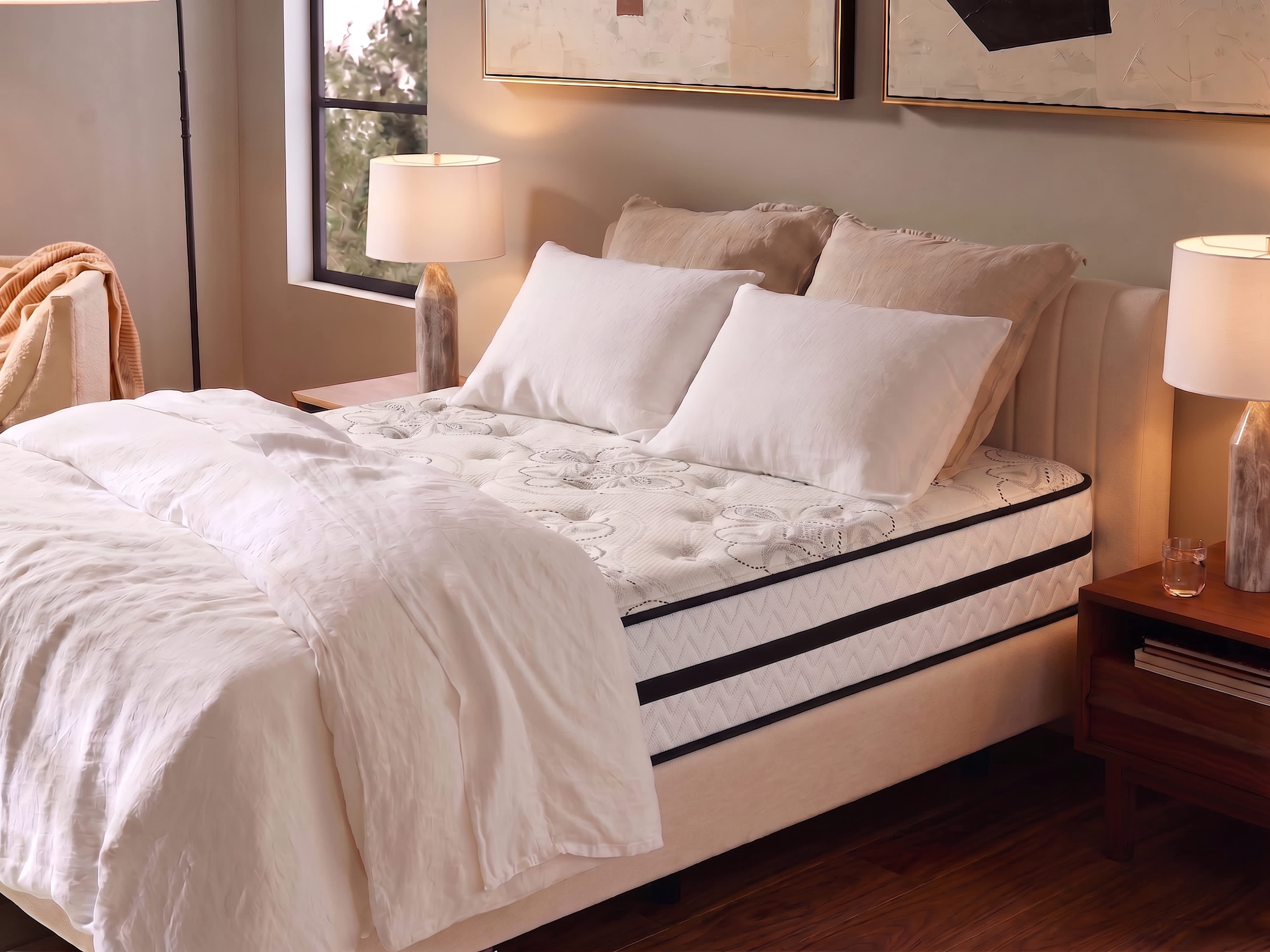 A Hybrid mattress with white bedding and pillows in a bedroom with two lamps and artwork.