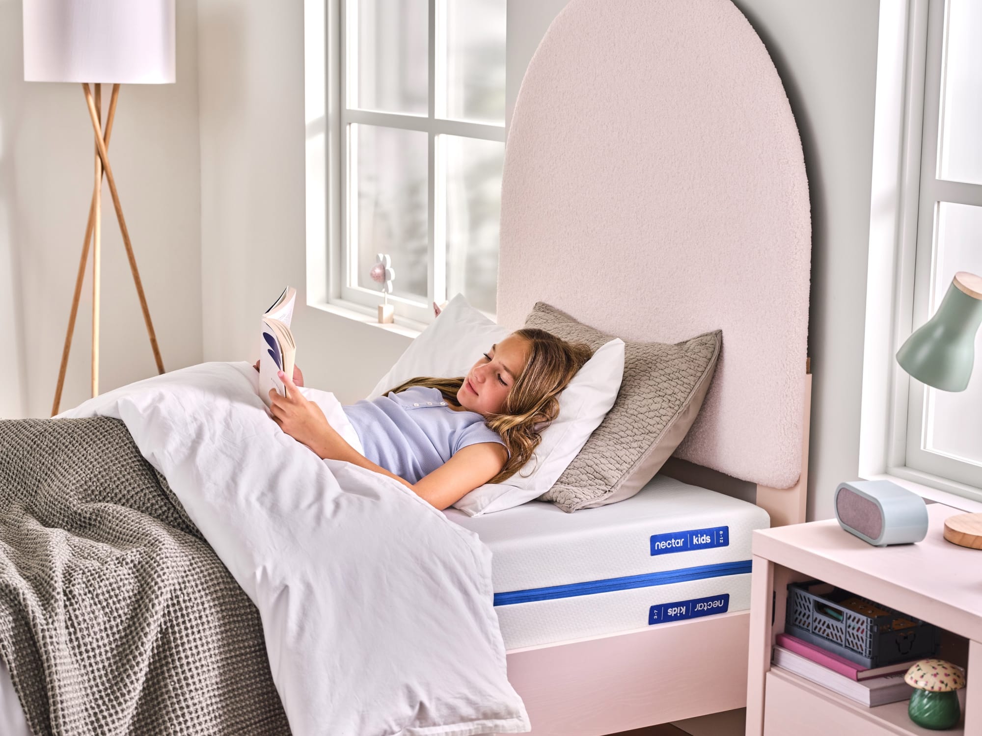 girl lying in bed on her Nectar Kids mattress reading a book