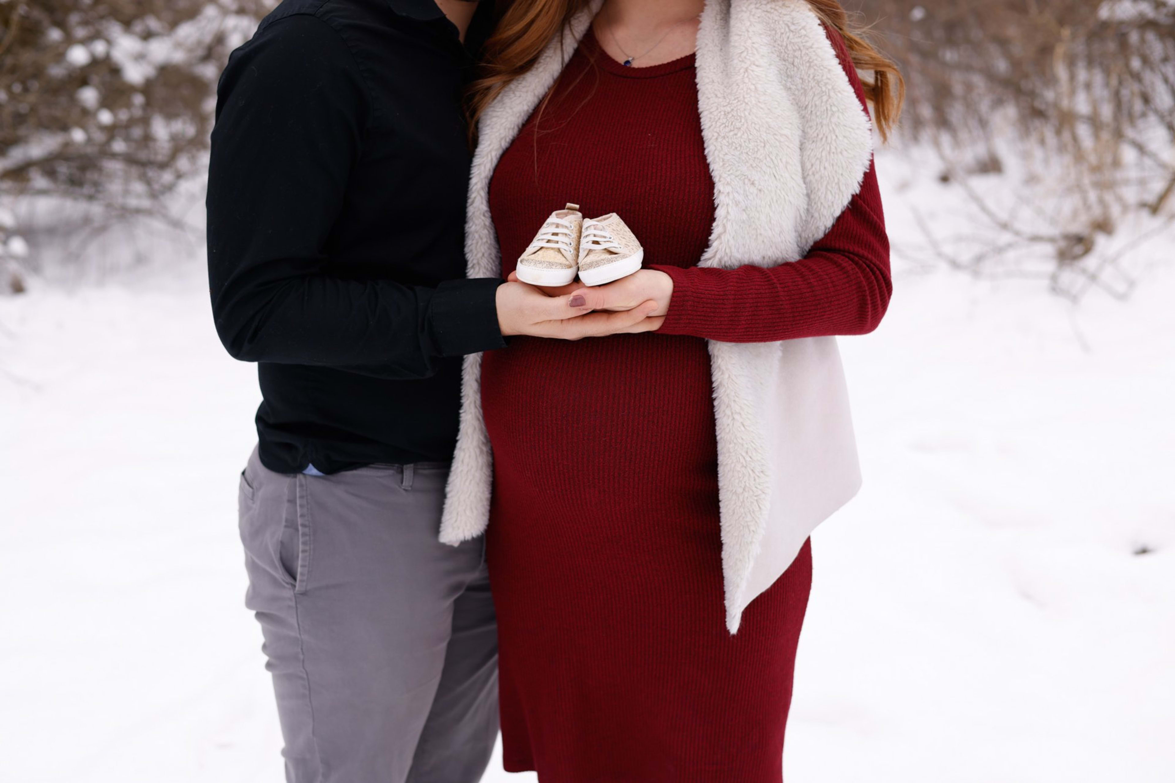 Expecting couple holding tiny baby shoes over the bump in the snow, Metro Detroit maternity session