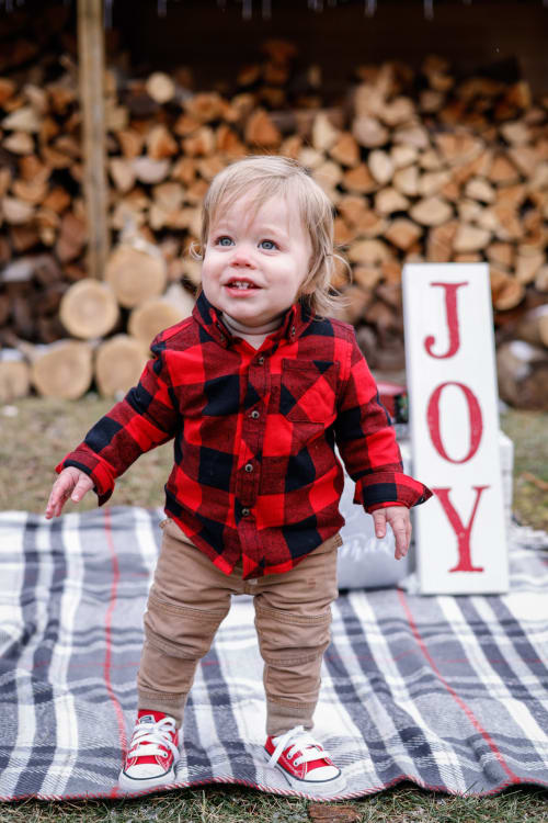 Toddler in buffalo plaid beside a JOY sign and woodpile, Metro Detroit Christmas mini session