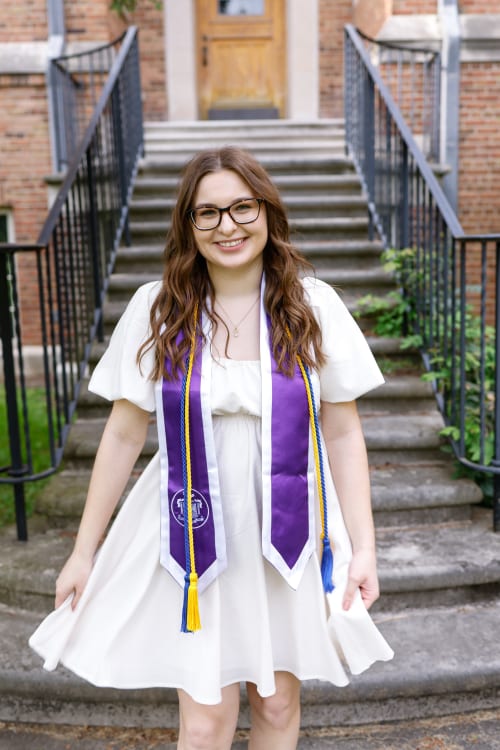 College graduate in a white dress and honor stole on stone steps, Metro Detroit graduation session