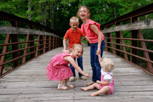 Siblings laughing together on a wooden bridge, southeast Michigan family session