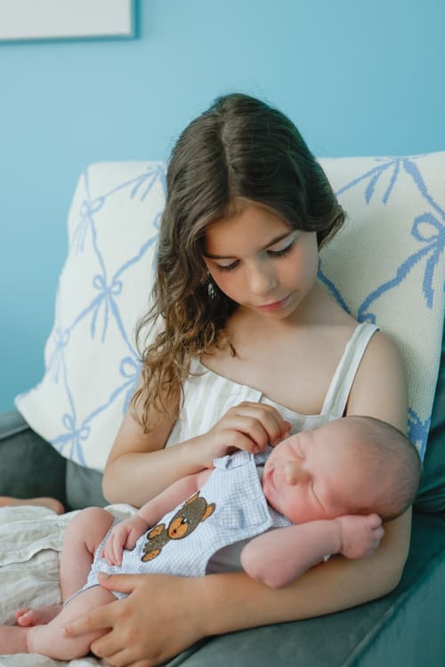Big sister cradling her newborn sibling in a chair, Metro Detroit newborn session