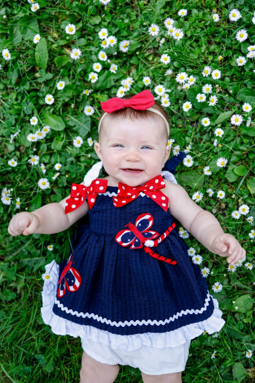 Baby girl in a patriotic dress lying among daisies, southeast Michigan summer session