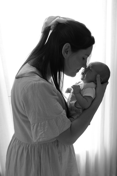 Black-and-white photo of a mother nuzzling her newborn by the window, Metro Detroit newborn session