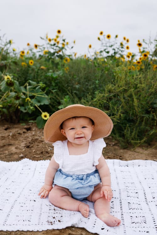 Baby girl in a straw hat sitting in a sunflower field, Metro Detroit sitter session