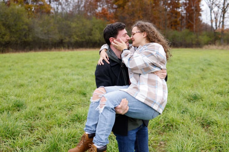 Newly engaged John lifting Katy for a kiss in a golden autumn field