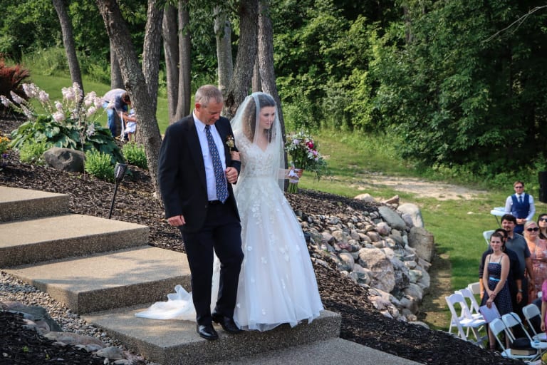 Quintanya walks down the stairs in her blusher veil on her father's arm