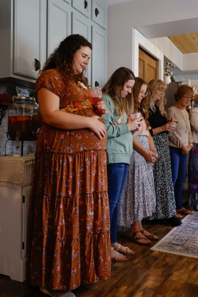 Guests bow their heads in prayer over the mom-to-be at the baby shower