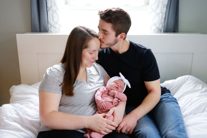 Parents kissing while holding their newborn daughter in a pink wrap, Metro Detroit newborn session