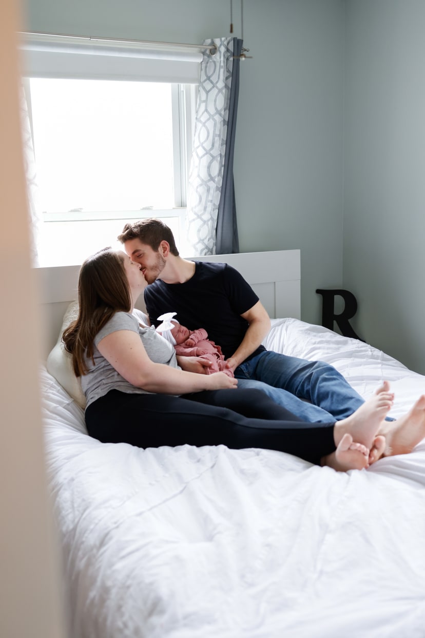 Parents kissing over their newborn on a bed, Metro Detroit newborn session