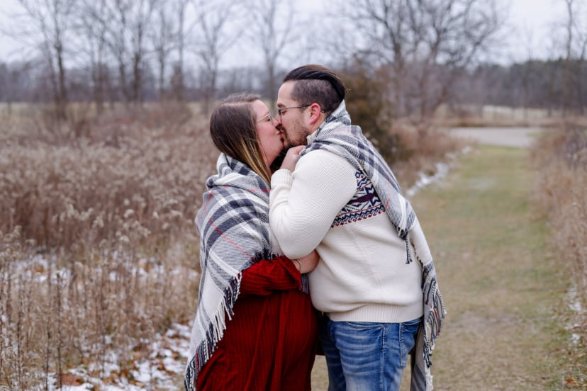 Couple kissing under a plaid blanket in a winter field, southeast Michigan Christmas mini session