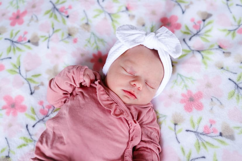 Sleeping newborn girl in pink with a bow headband on a floral blanket, Metro Detroit newborn session