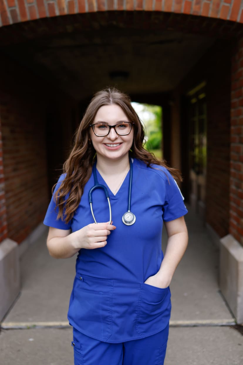 Nursing graduate in blue scrubs with a stethoscope in a brick breezeway, Metro Detroit graduation session