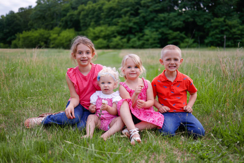 Four young siblings sitting together in a grassy field, Metro Detroit family session