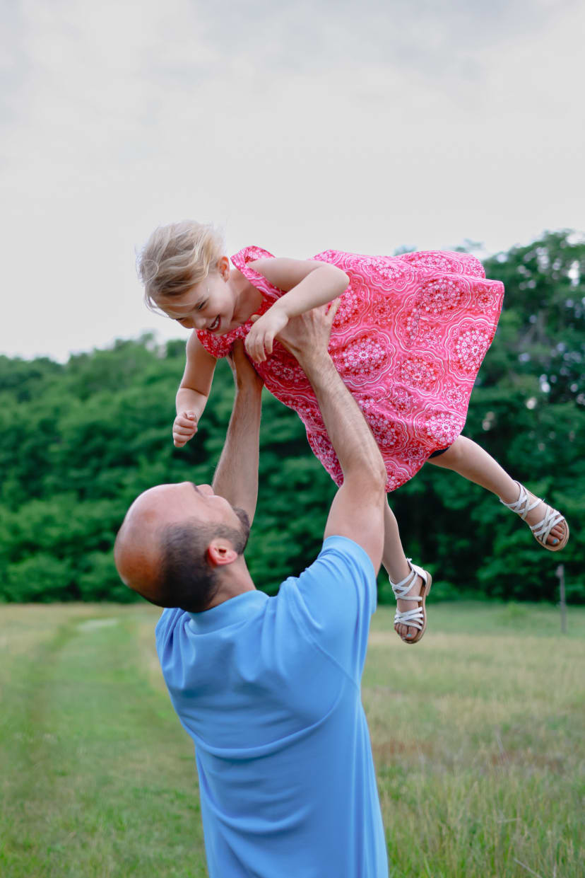 Father lifting his laughing daughter into the air in a field, southeast Michigan family session