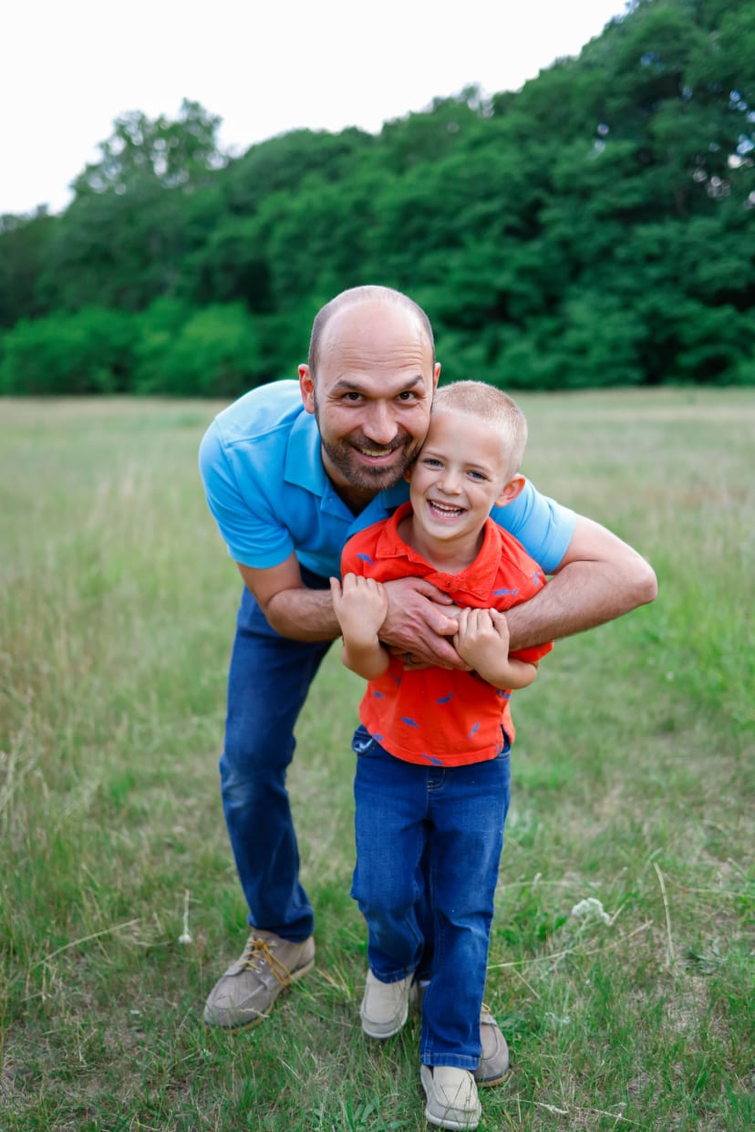 Father hugging his young son in a grassy field, southeast Michigan family session