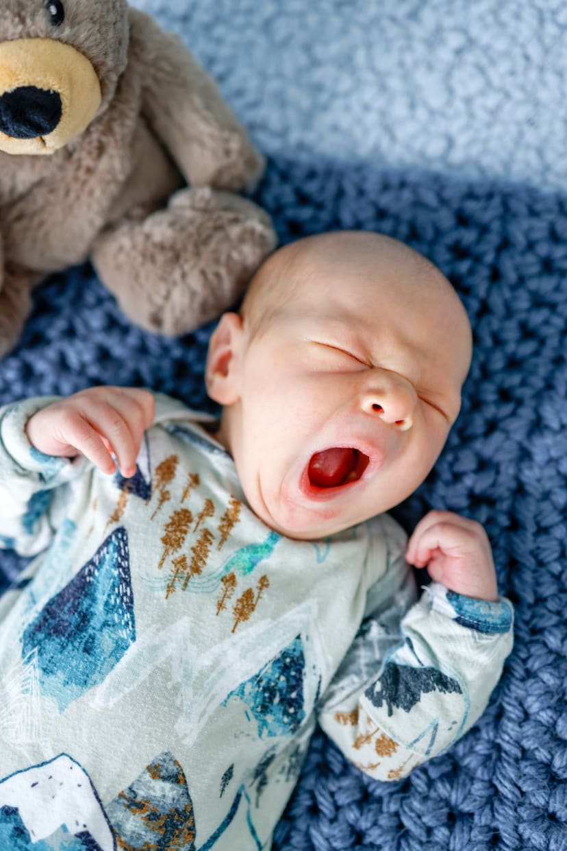 Newborn yawning in a mountain-print outfit on a blue blanket, Metro Detroit newborn session