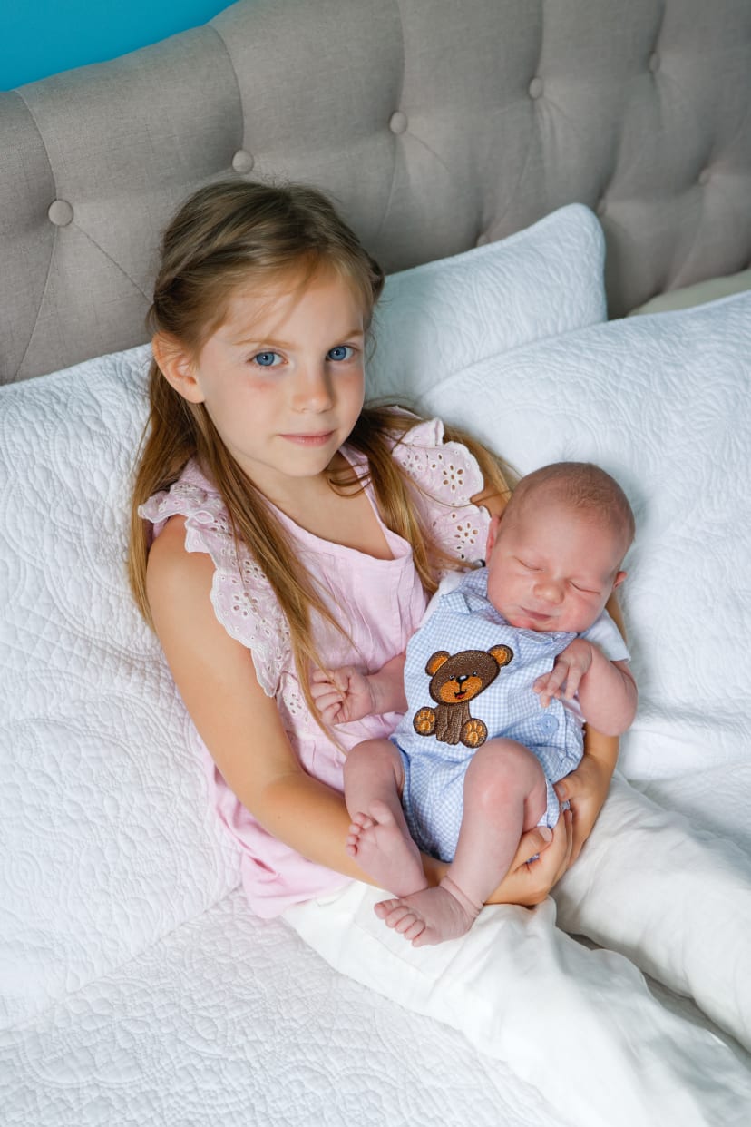 Big sister holding her newborn sibling on a bed, Metro Detroit newborn session