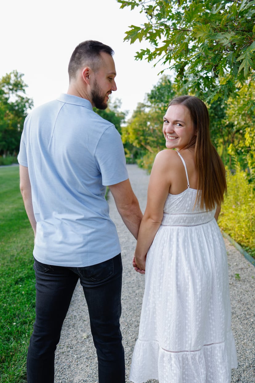 Couple holding hands on a garden path as she glances back, southeast Michigan engagement