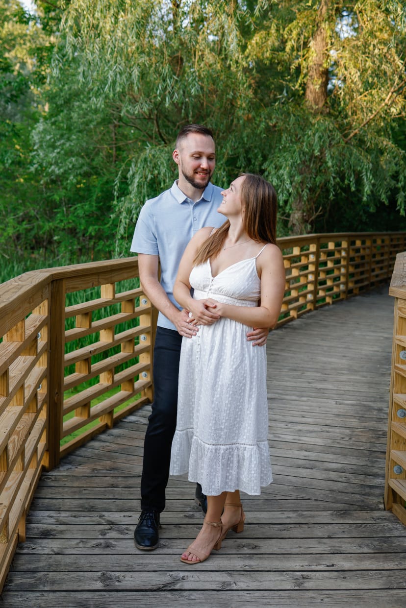 Couple standing close on a wooden footbridge surrounded by greenery, southeast Michigan engagement