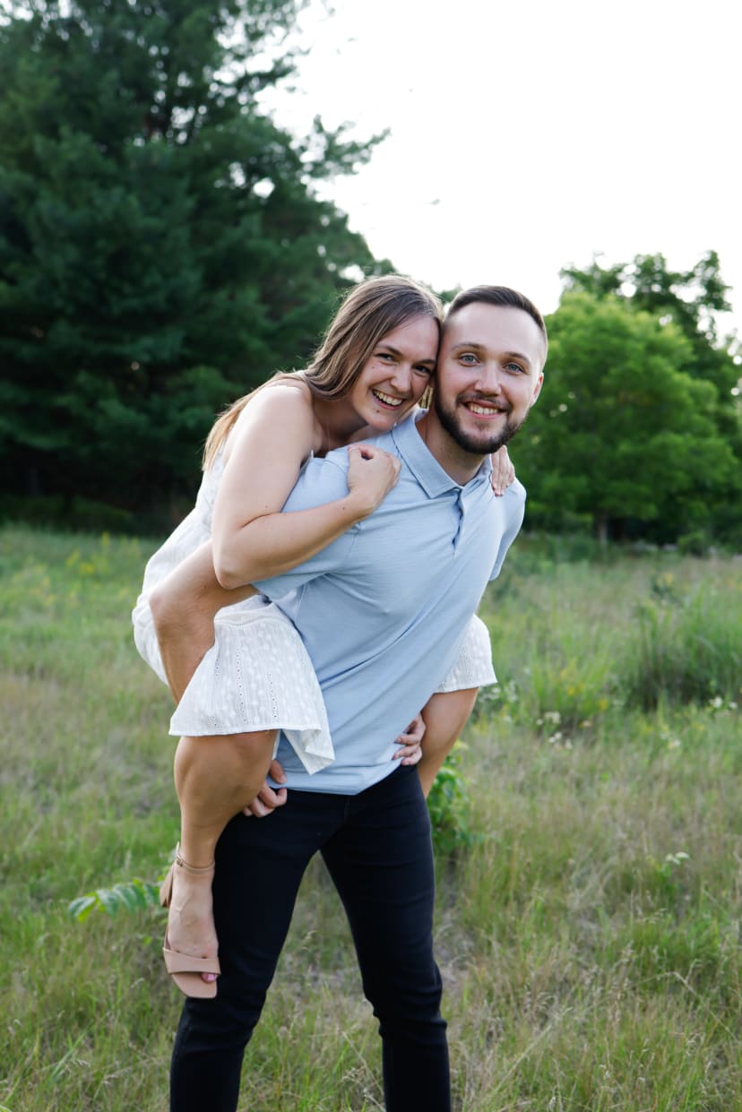 Man giving his fiancee a piggyback ride in a field, southeast Michigan engagement