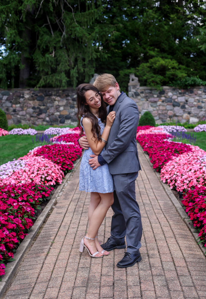 Couple embracing on a flower-lined garden path, Metro Detroit engagement session