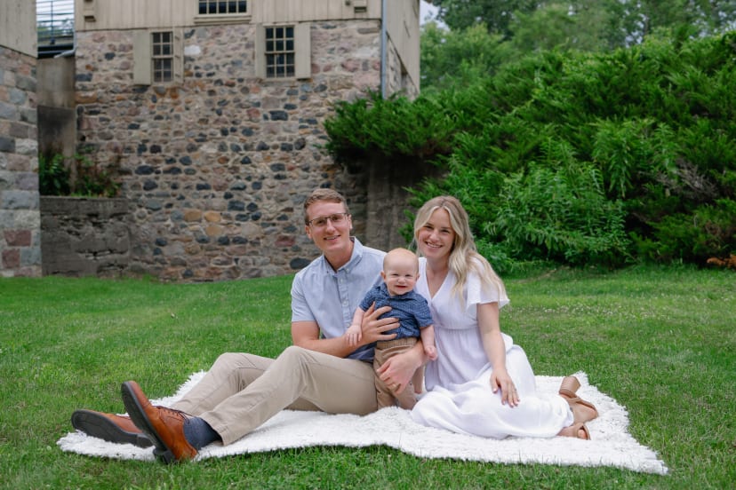 Family sitting on a blanket with their baby by a stone wall, southeast Michigan family session