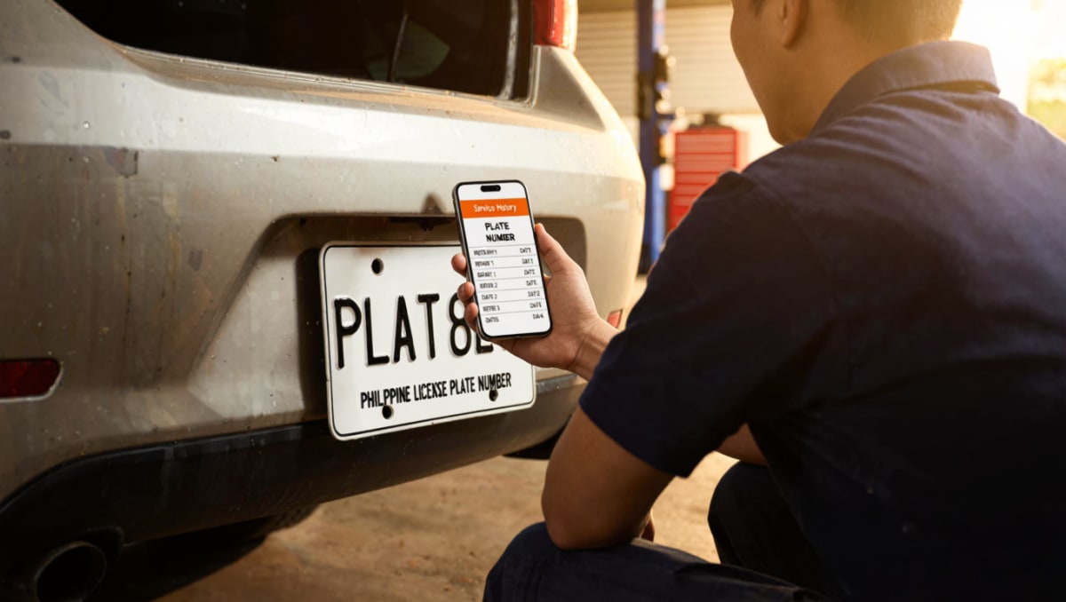 Mechanic holding a phone beside a car's license plate, showing that vehicle's full service history in auto repair shop software