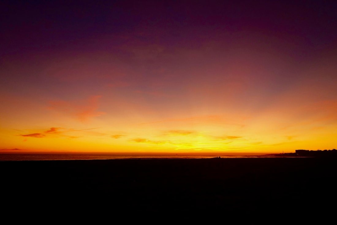 Orange and purple sunset over the empty sand at Praia de Carcavelos near Lisbon