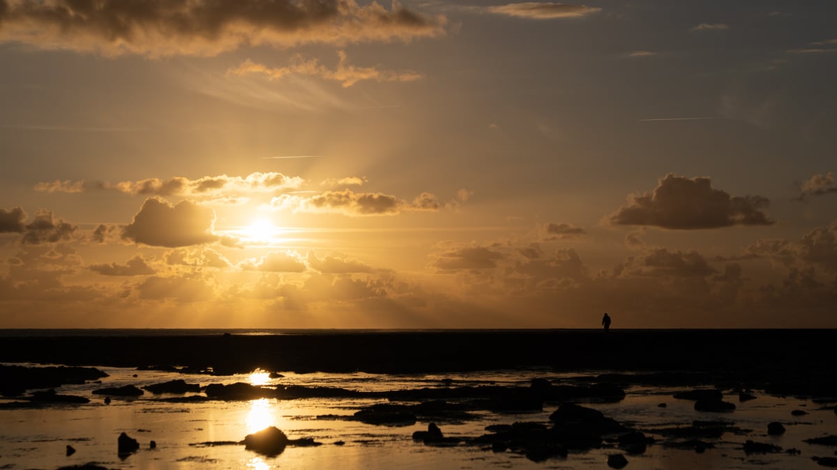 Soleil bas et doré au-dessus de la mer à marée basse, une silhouette au loin sur l'horizon
